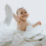 A baby is laying on the bed and smiling.